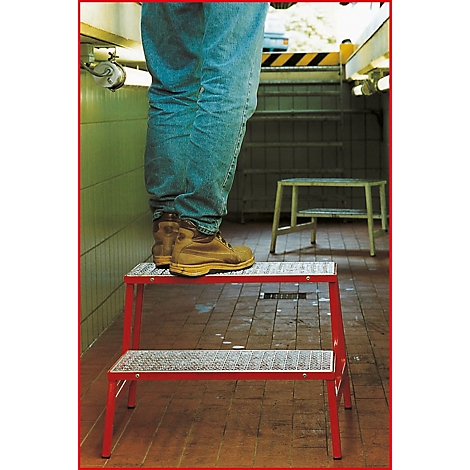 Person steht auf roter Trittleiter in Waschraum. Braune Stiefel, Jeans, Fliesen. Auf dem Boden, steht eine weitere Trittleiter.